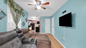 A living room with a sectional sofa, a ceiling fan, and a flat-screen TV mounted on the wall. - Cozy 1-bedroom apartment in gorgeous Hartford with AC (Hartford)