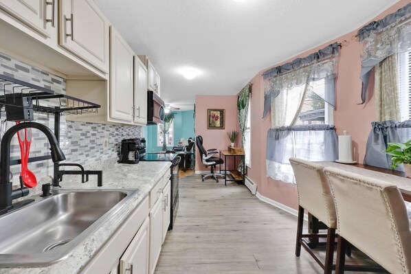 A kitchen with a sink, cabinets, and a dining area with chairs and a table.