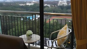 Un balcón con vistas a un paisaje urbano, una mesita con una planta y una silla con cojín.