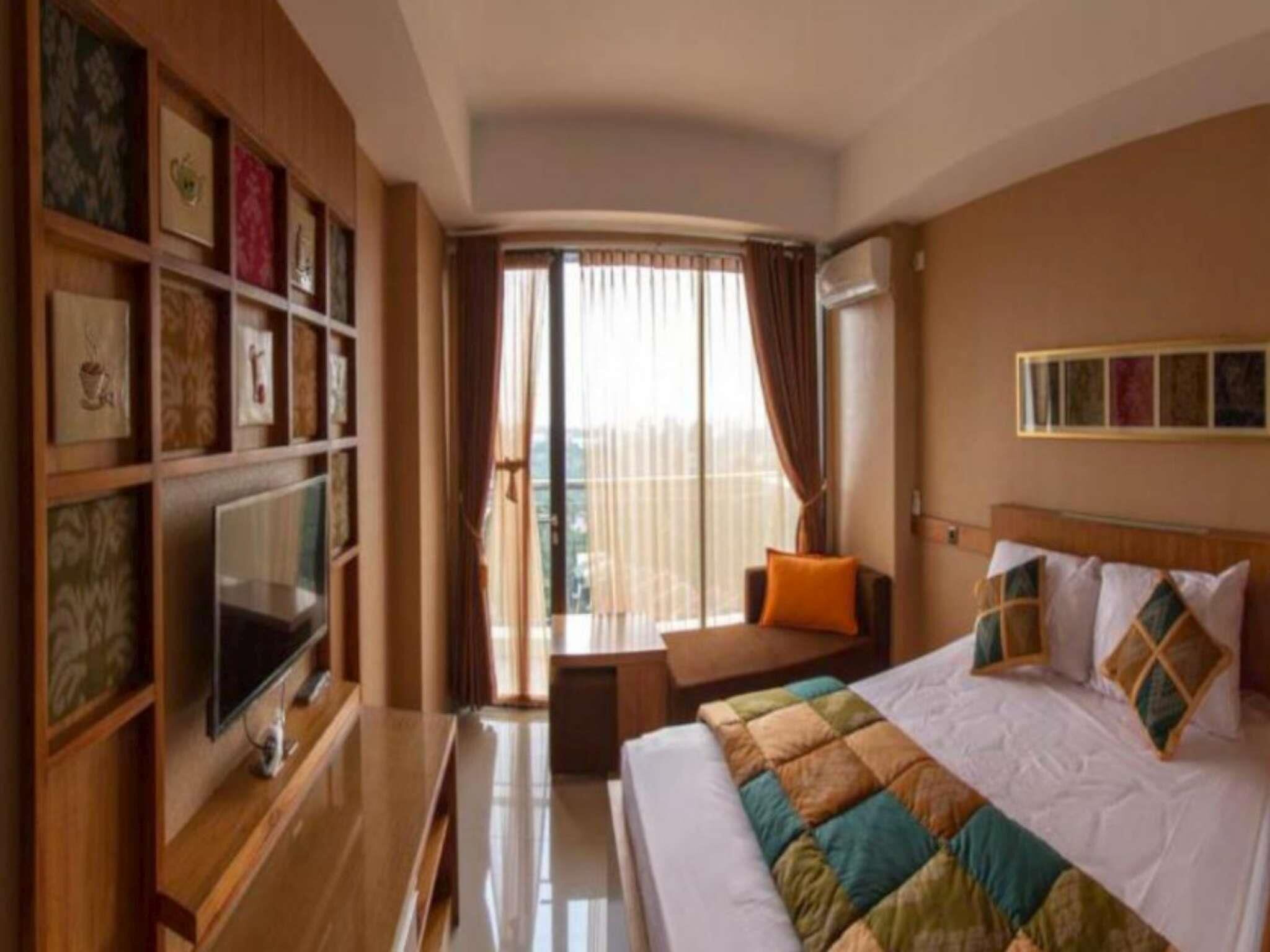 A hotel room with a bed, a TV, a desk, and a window with curtains.