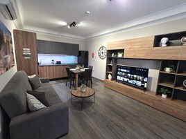 Una sala de estar moderna con un sofá, una mesa de centro, un televisor y una cocina al fondo.