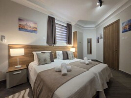 Un cuarto de hotel con una cama grande, dos mesitas de noche, un cabecero y obras de arte en las paredes.
