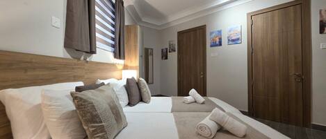 Habitación de hotel con dos camas, cabecera de madera, un espejo grande y una ventana con cortinas.