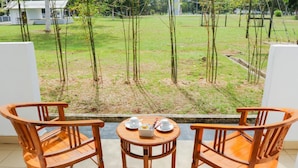 A balcony with two wooden chairs and a small table, overlooking a grassy area with young trees and a white building in the background. - The Payang Scout Hotel (Kuala Terengganu)