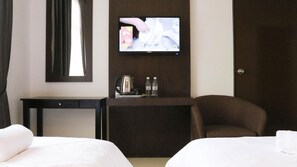 Una camera d'albergo con due letti, una TV fissata al muro, un tavolino con una macchina da caffè e bottiglie d'acqua, e una sedia.