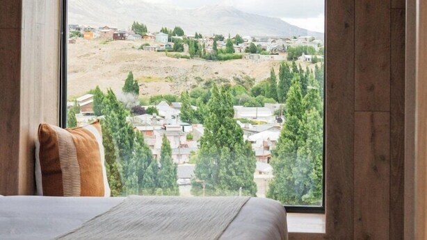 Ein Schlafzimmer mit großem Fenster, Holzwänden, einem Bett und Blick auf eine Stadt und Berge.