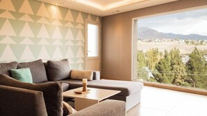 Ein modernes Wohnzimmer mit einer Eckcouch, einem kleinen Couchtisch und einem großen Fenster mit Blick auf eine Berglandschaft.