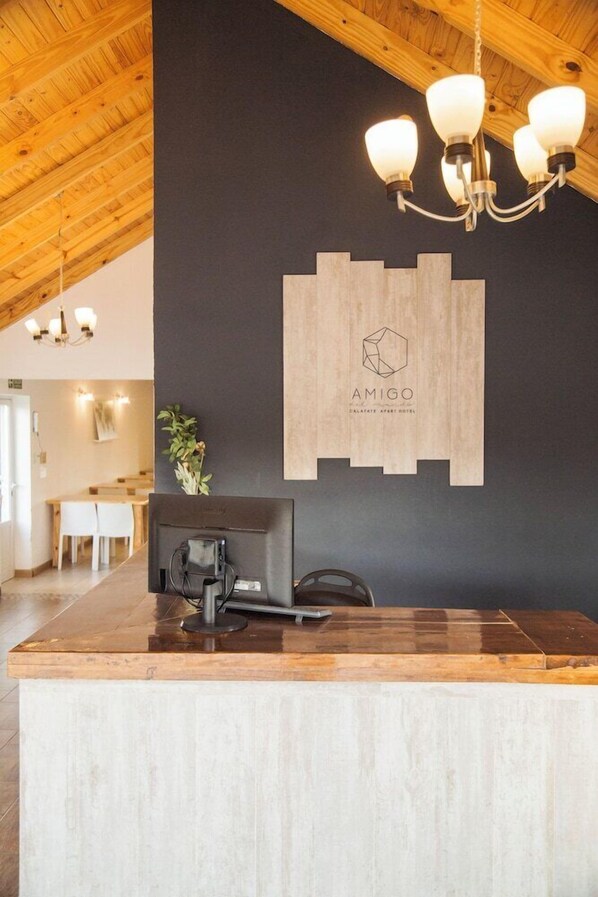 Un comptoir d’accueil en bois, un mur noir orné d’un logo et un lustre.