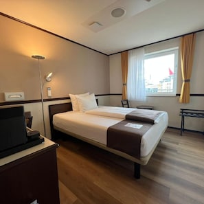 A hotel room with a bed, bedside table, lamp, and a window with curtains. - Toyoko Inn Frankfurt Am Main Hauptbahnhof (Frankfurt)