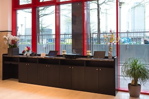 A reception desk with a laptop, phone, and flowers. There are large windows with a view of the outside. - Toyoko Inn Frankfurt Am Main Hauptbahnhof (Frankfurt)