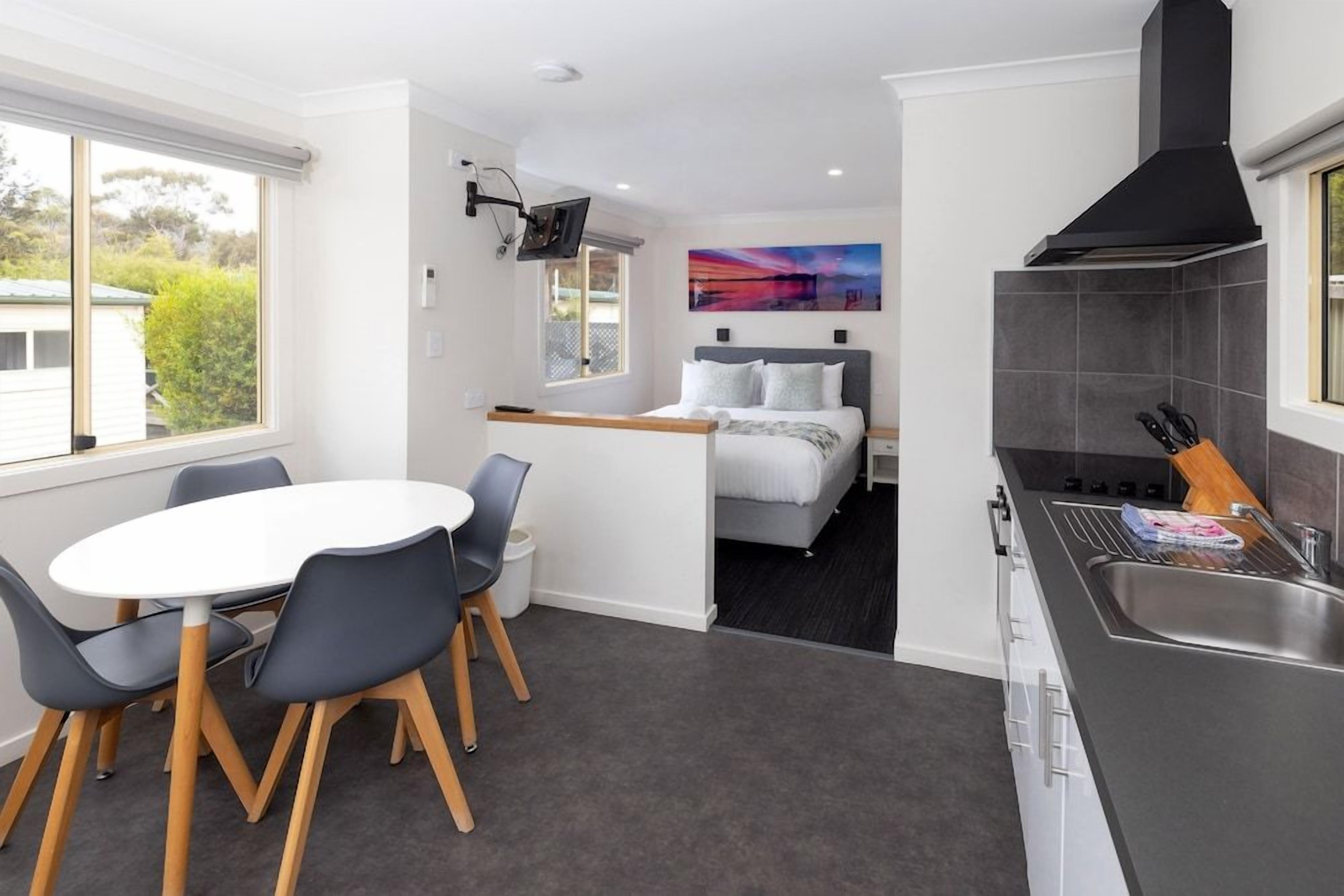A compact hotel room with a dining area, a bed with a view, and a kitchenette.
