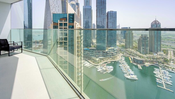 Un balcon situé dans un immeuble de grande hauteur, doté d’une rambarde en verre, qui offre une vue sur un port de plaisance et sur le panorama urbain.