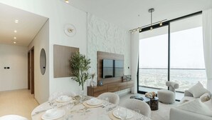 Ein modernes Wohnzimmer mit Essbereich, einem großen Flachbildfernseher an einer strukturierten Wand und Blick auf die Stadt durch große Fenster.