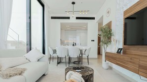 Ein modernes Wohnzimmer mit einer Couch, einem Couchtisch mit Decke, einem Essbereich mit Tisch und Stühlen sowie einem Fernseher auf einer Holzkommode.