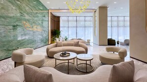 Eine moderne Lobby mit einer gebogenen Sofagruppe, einer Kristallleuchtre und einer Marmorwand mit einem Logo.