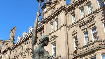A statue of a woman holding a lamp in front of a large, ornate building with classical architecture.