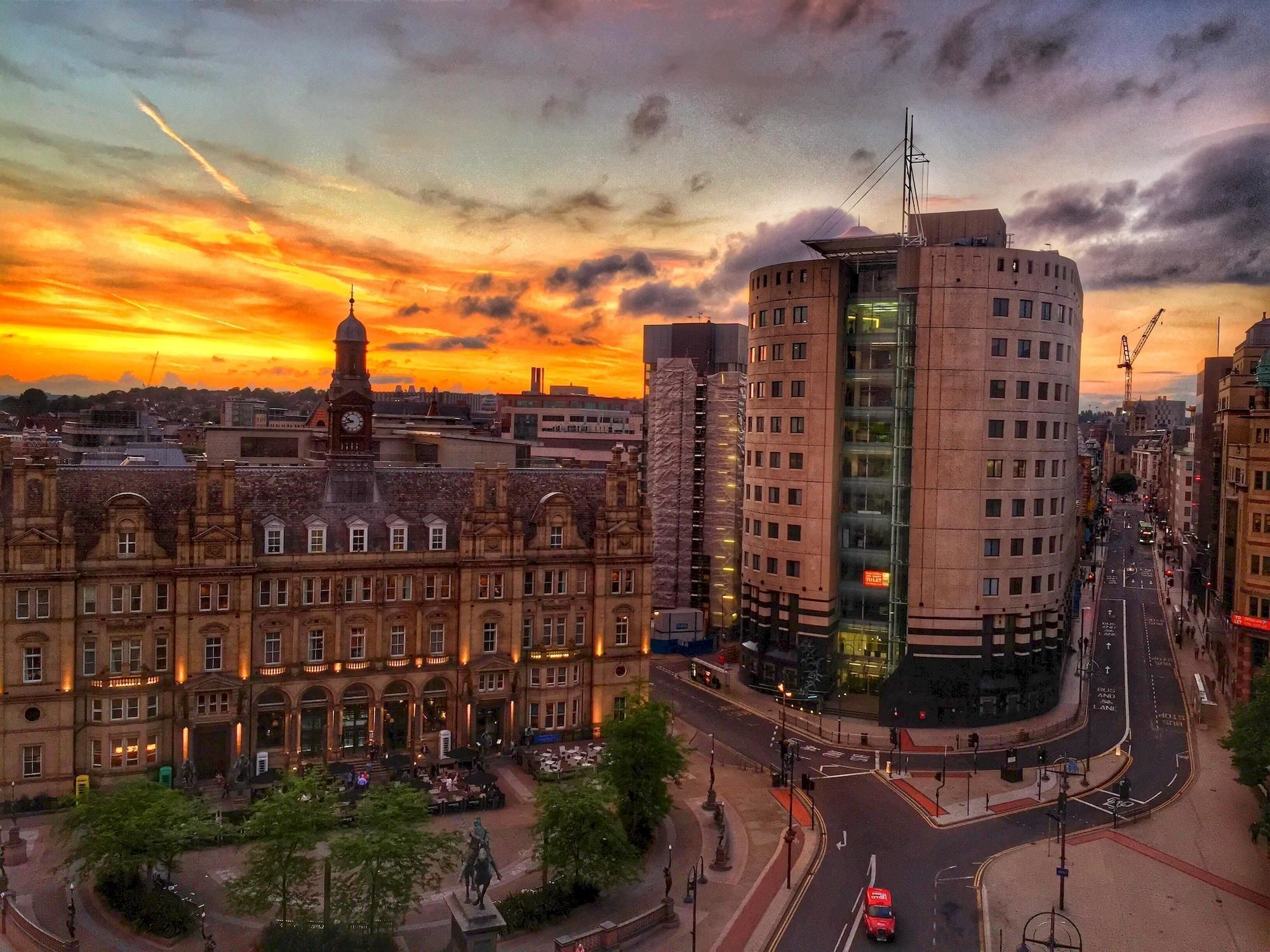 A historic building with a clock tower, surrounded by modern high-rise buildings and a busy intersection.