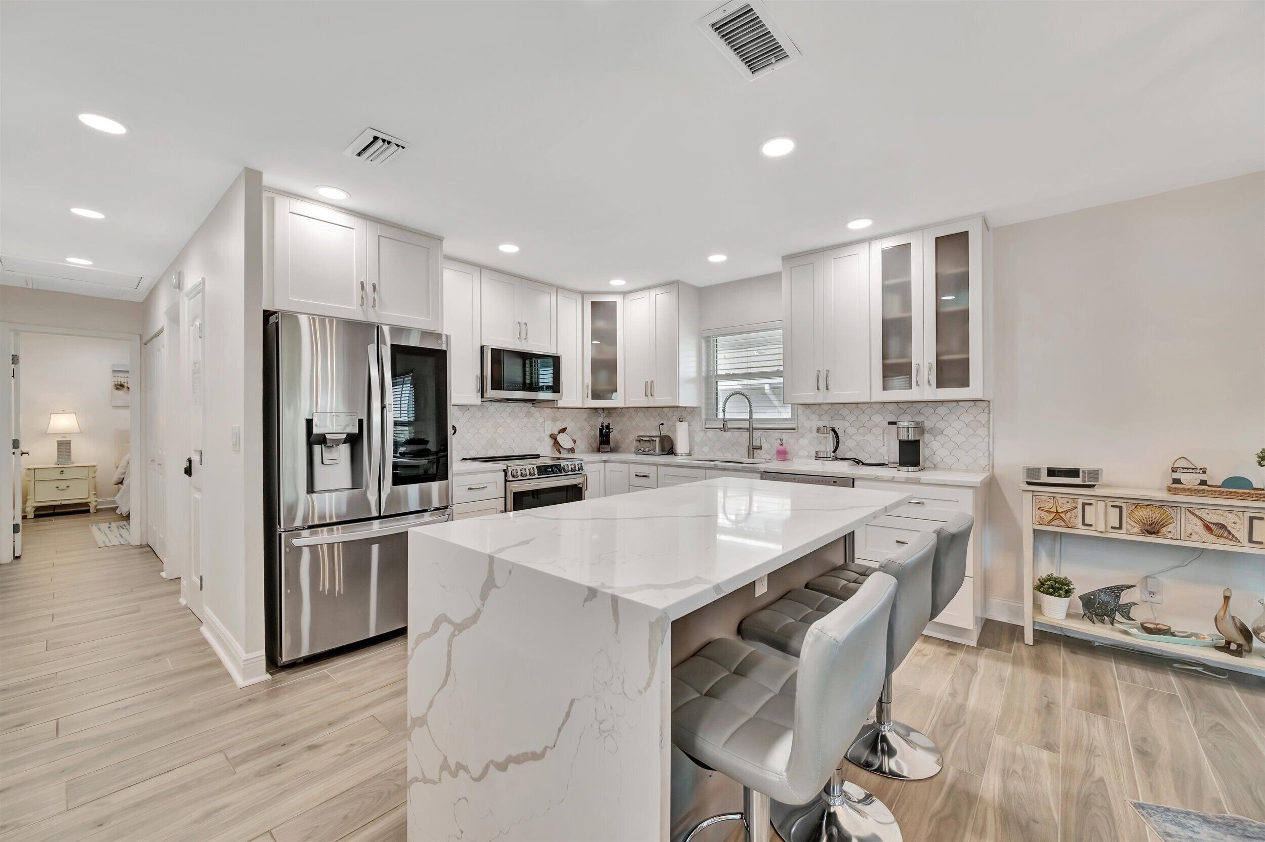A modern kitchen with white cabinetry, stainless steel appliances, and a marble island with bar stools.