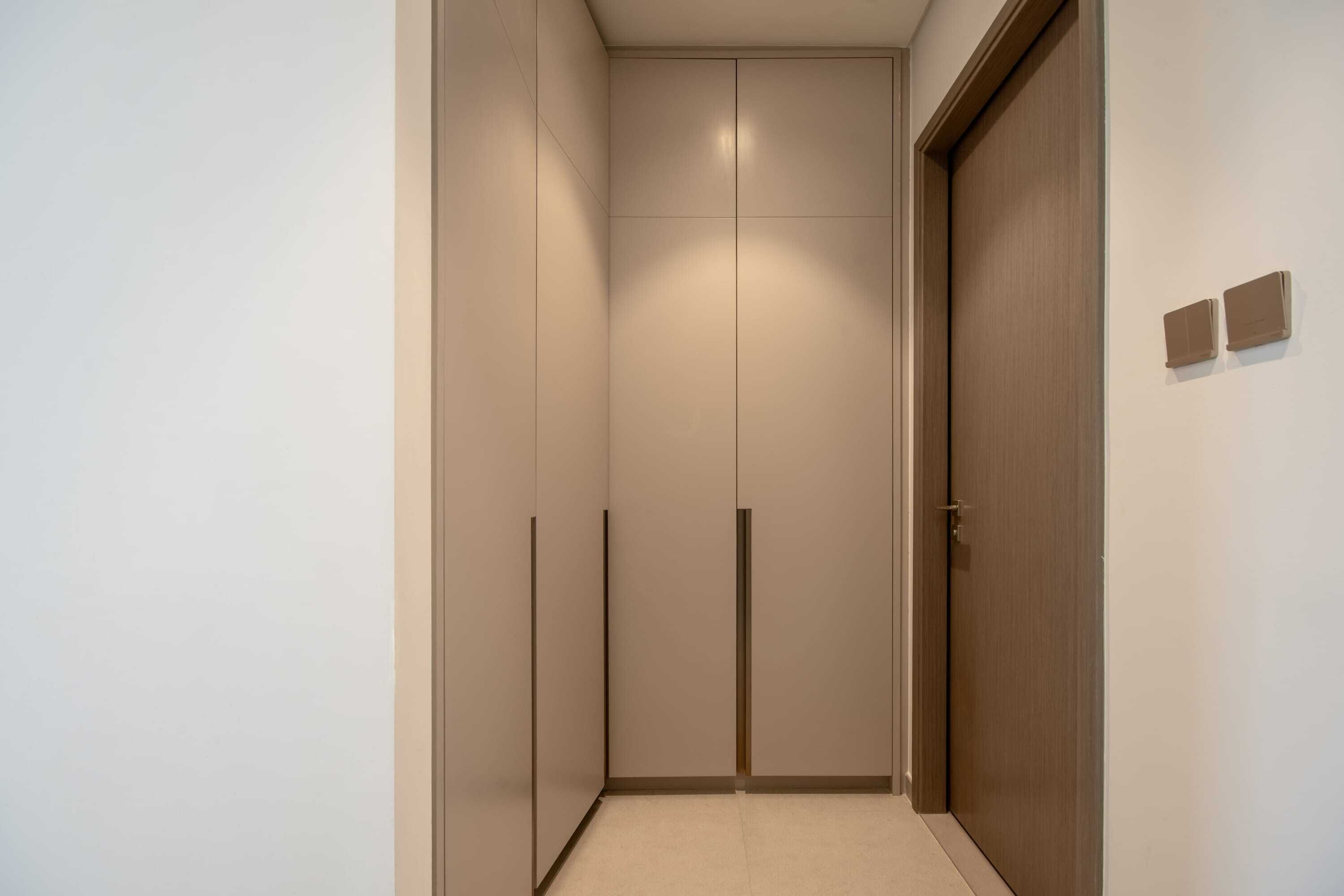 A narrow hallway with a wooden door at the end, a light switch, and a small wall-mounted control panel.