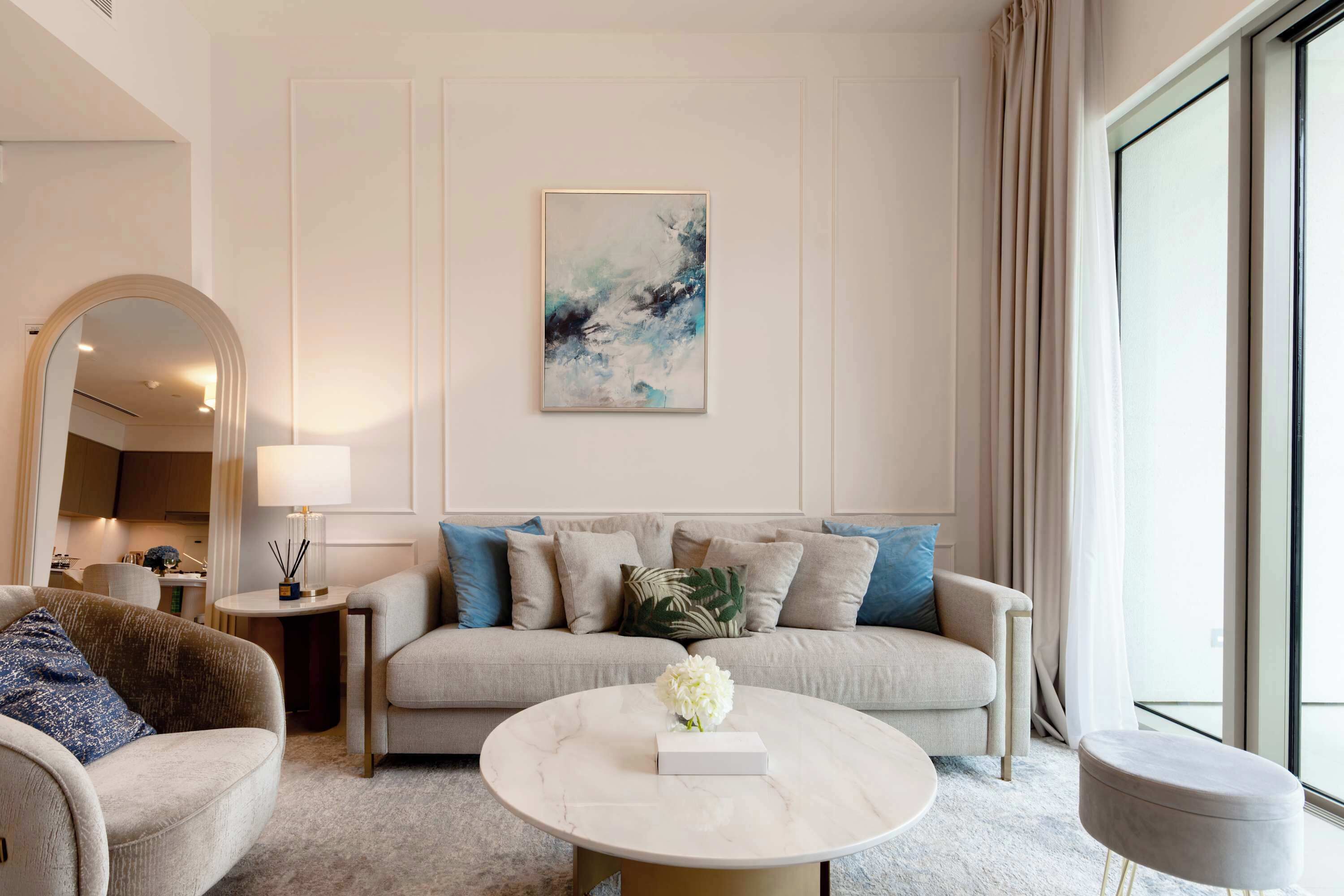 A modern living room with a sofa, armchairs, a round coffee table, and a large window with curtains.