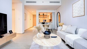Una sala de estar moderna con sofá, mesa de centro y televisor. Se observa un área de cocina al fondo.