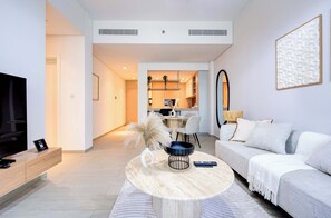 A modern living room with a sofa, coffee table, and TV. There is a kitchen area in the background. - Luxury Furnished 1BR, Prime Location, Al Meydan (Dubai)
