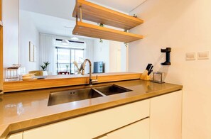 A modern kitchen with a double sink, wooden shelves, and a view into the living area. - Luxury Furnished 1BR, Prime Location, Al Meydan (Dubai)