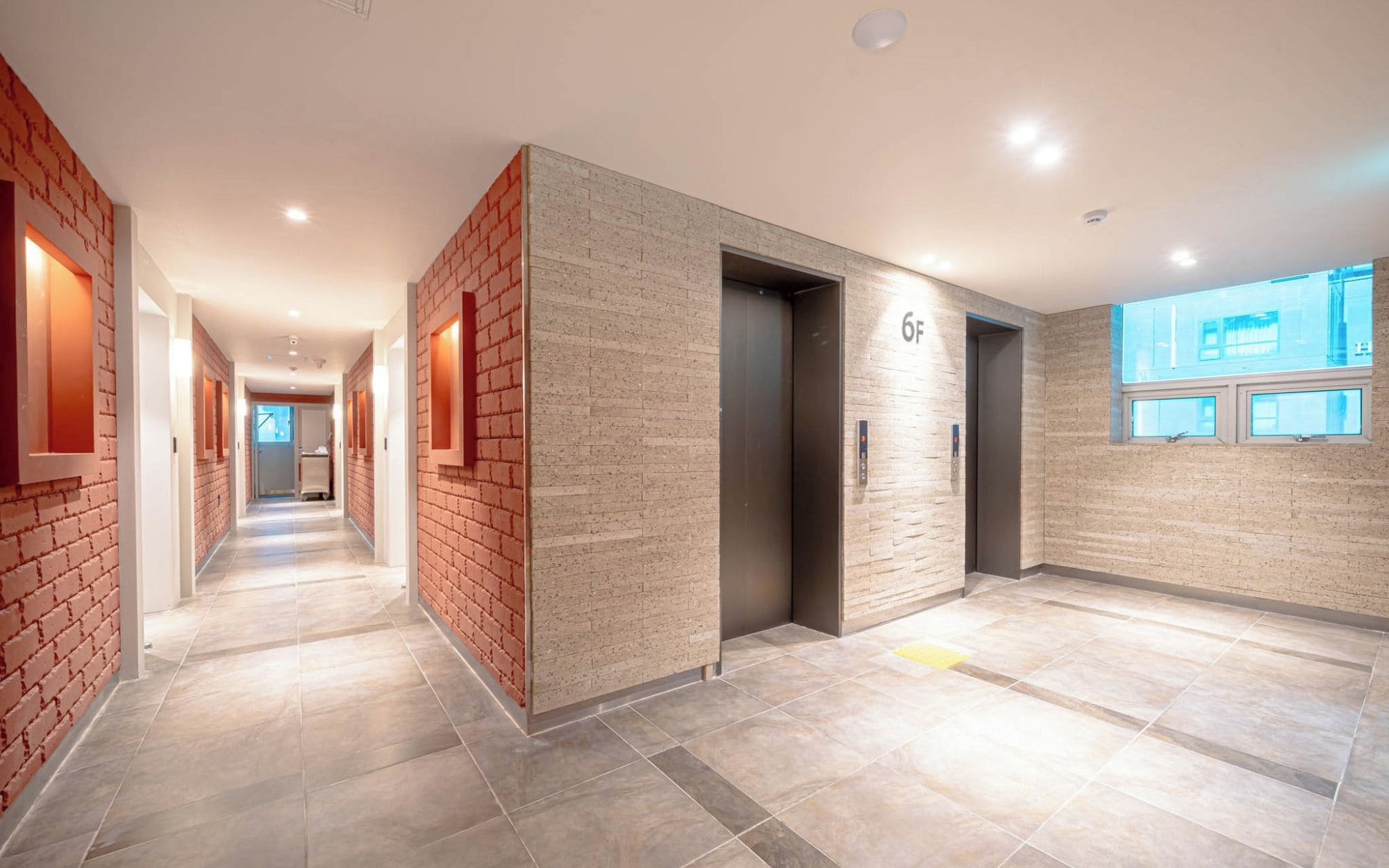 A modern hotel corridor with a brick accent wall, an elevator, and a view of the outside.