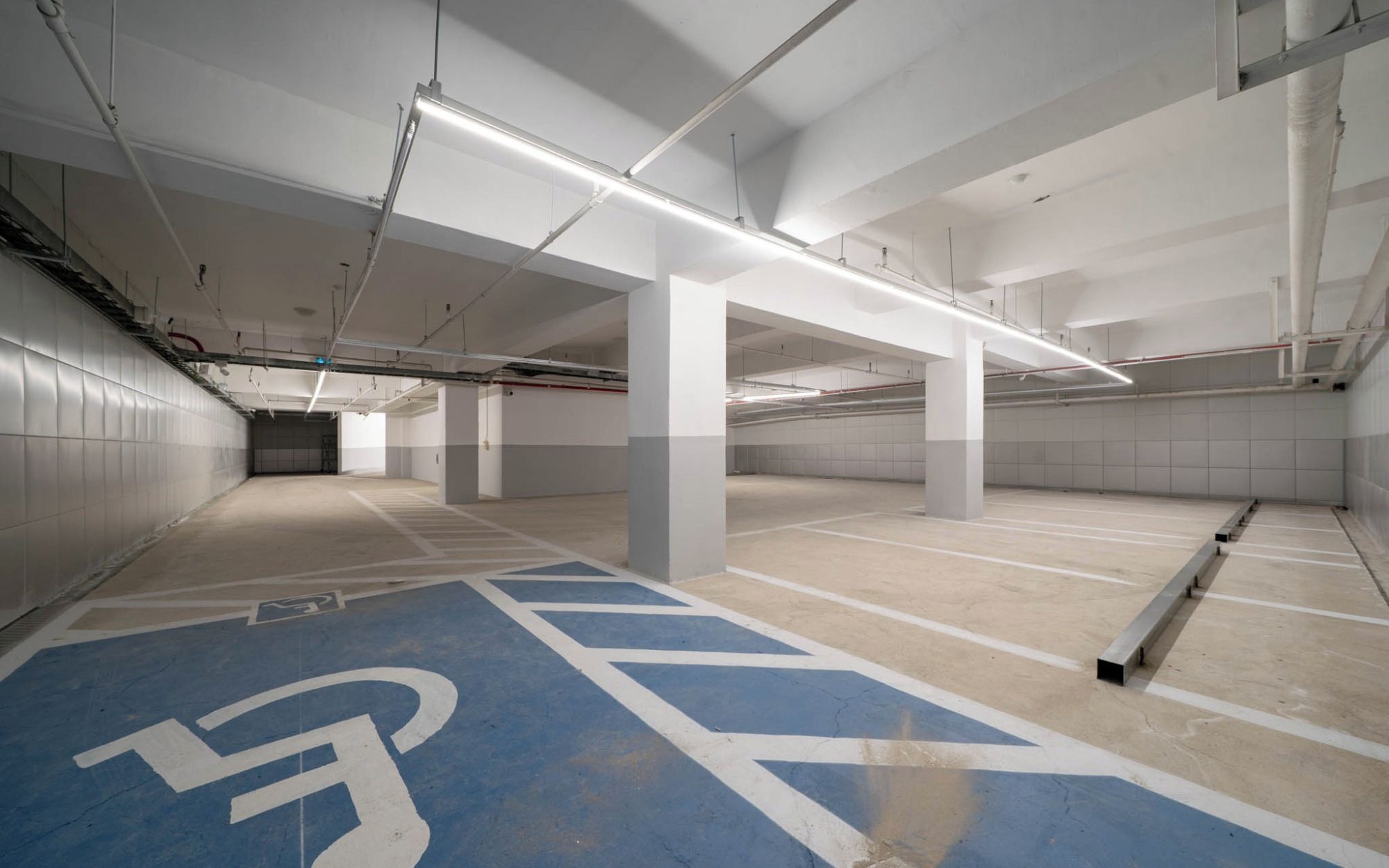 An empty parking garage with white pillars, fluorescent lighting, and blue handicapped parking spaces.