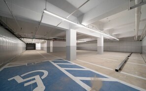 An empty parking garage with white pillars, fluorescent lighting, and blue handicapped parking spaces. - Ulsan Hound Hotel Samsan (Ulsan)