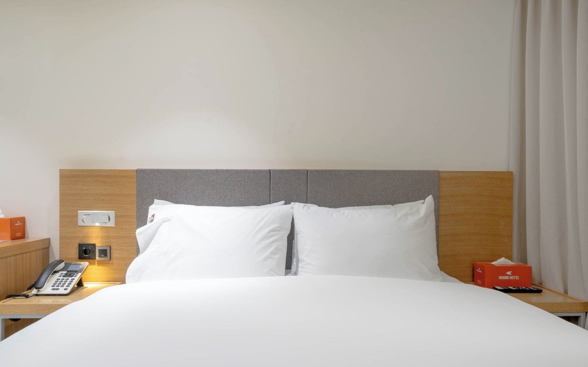 A hotel room with a bed, a bedside table with a phone, a tissue box, and a remote control.