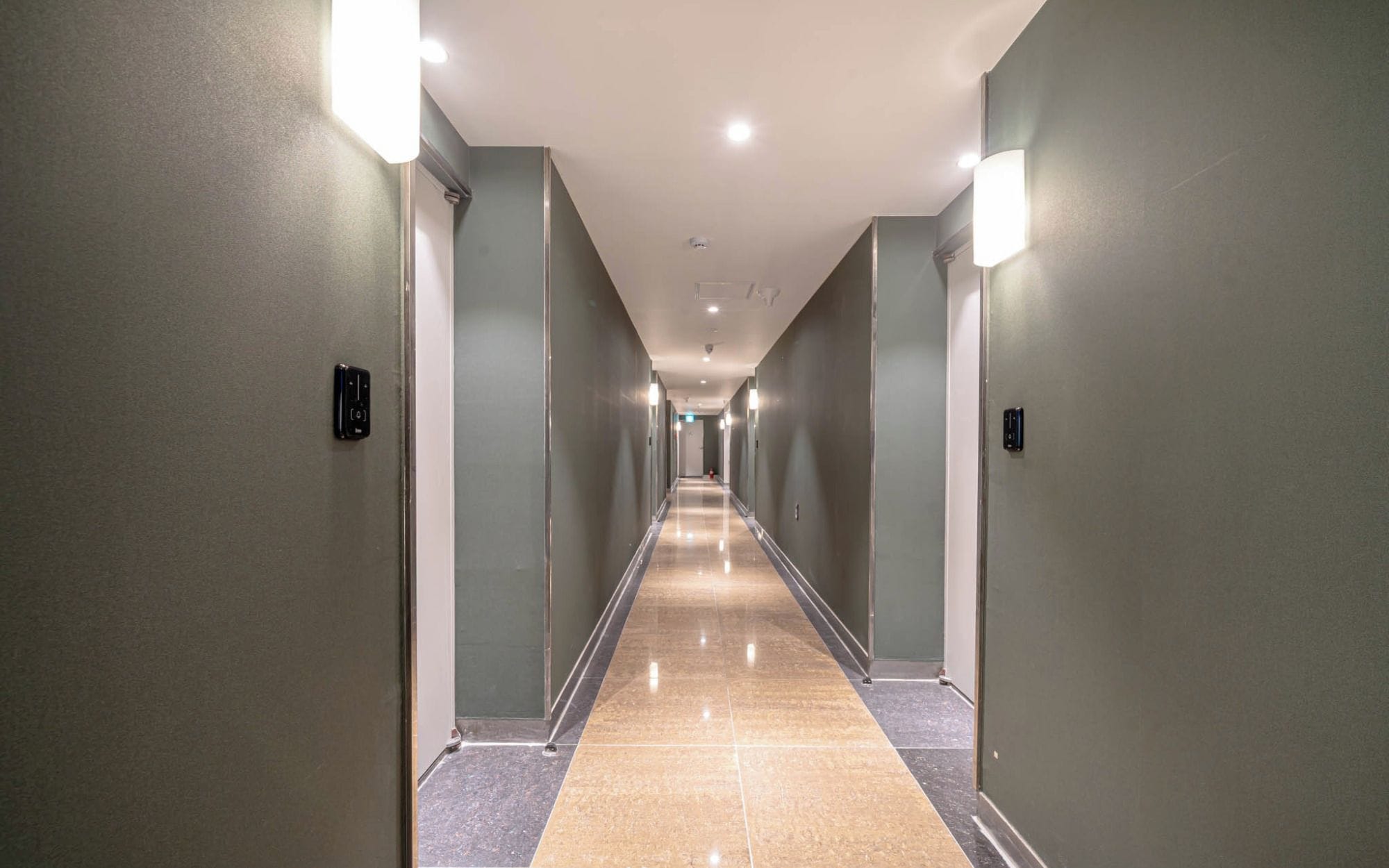 A long, narrow hotel corridor with a tiled floor and walls painted in a muted green.