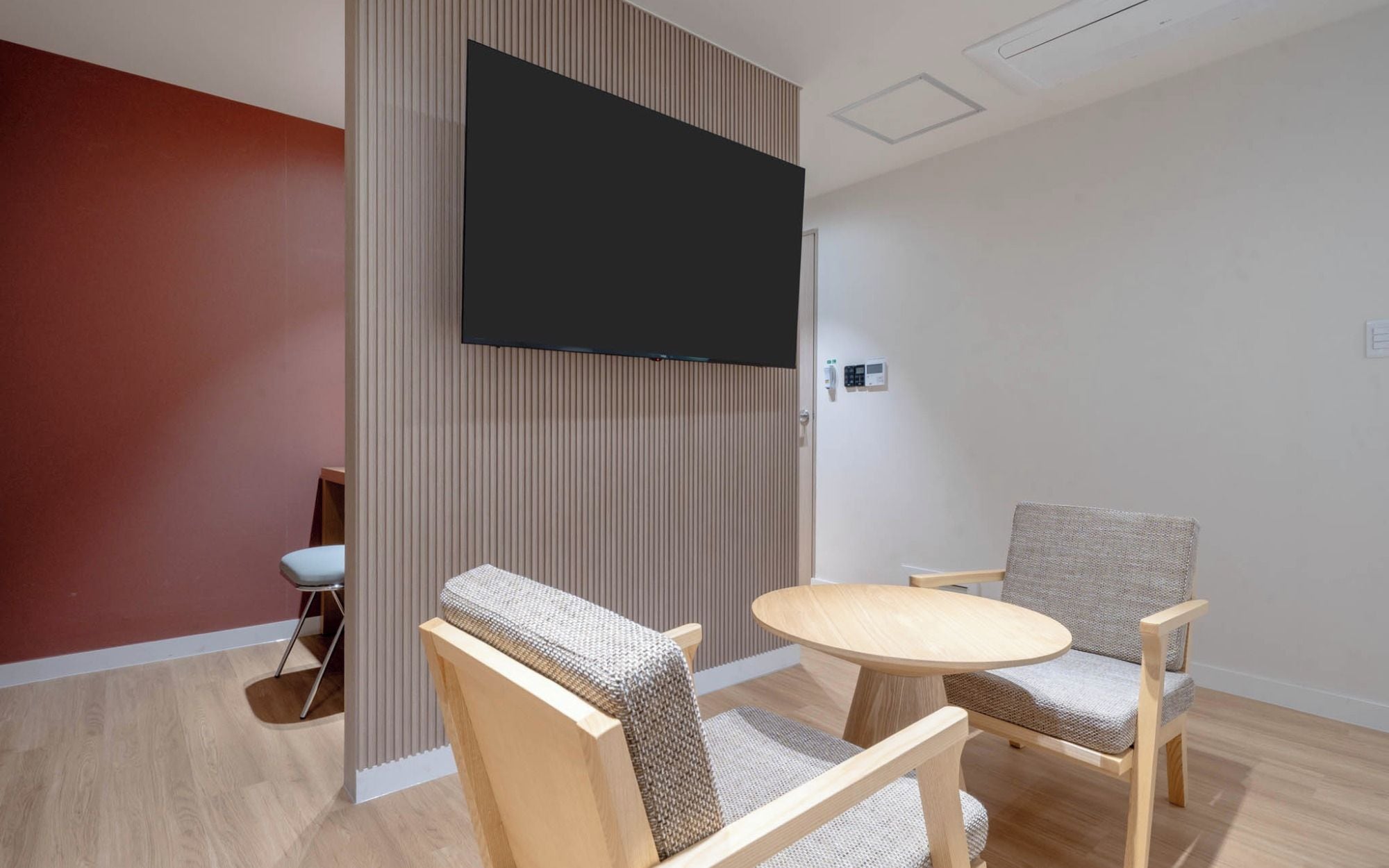 Habitación moderna con televisor de pantalla plana en la pared, dos sillones tapizados, una pequeña mesa redonda y una pared de acento en rojo.