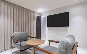 A modern hotel room with a flat-screen TV mounted on the wall, a grey upholstered sofa, a wooden coffee table, and a wardrobe. - Ulsan Hound Hotel Samsan (Ulsan)