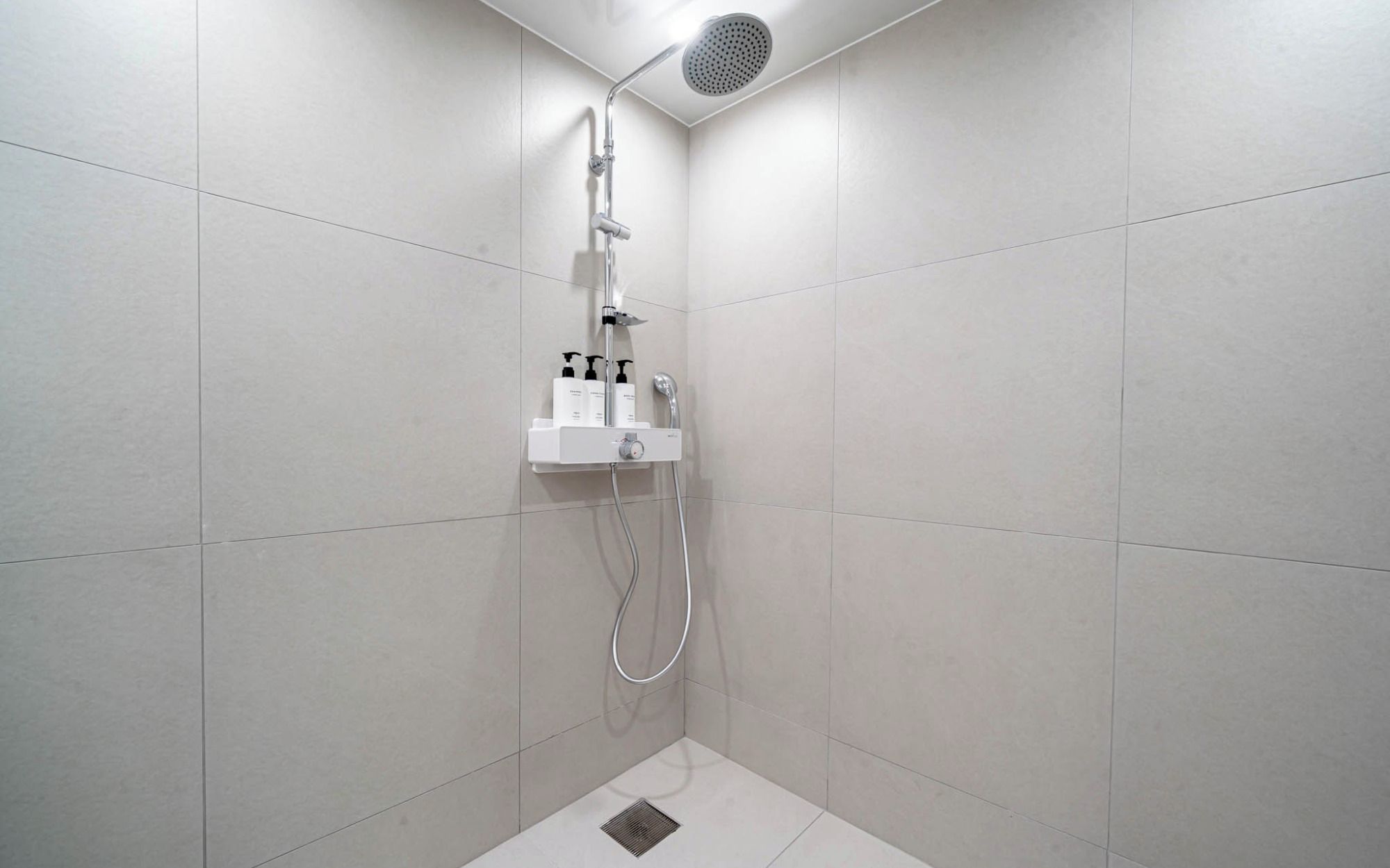 Ducha moderna con cabezal de ducha manual, panel de control en la pared y manguera para ducha de mano.