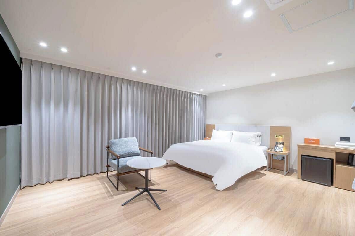 Una habitación de hotel moderna con una cama, un escritorio, una silla, un televisor y un minibar.