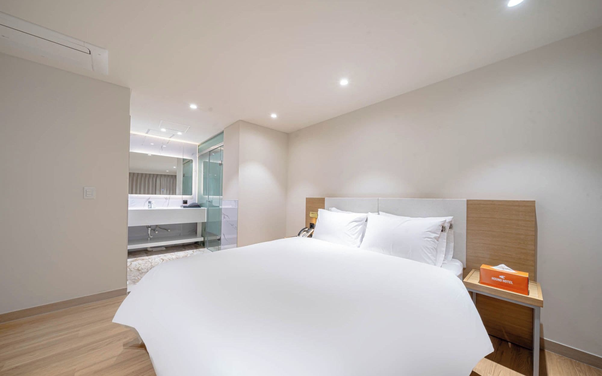 A hotel room with a large bed, a bedside table with a tissue box, and a bathroom with a mirror and sink.