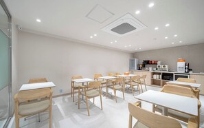 A modern dining area with multiple tables and chairs, a kitchen area with appliances, and a ceiling with recessed lighting. - Ulsan Hound Hotel Samsan (Ulsan)