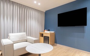 A modern hotel room with a sofa, a small round table, a flat-screen TV mounted on the wall, and a wooden cabinet with a towel and tissue box. - Ulsan Hound Hotel Samsan (Ulsan)