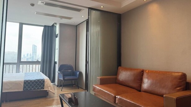 A modern hotel room with a bed, a leather sofa, a small table, and a chair. - Nomo Beijing Rd.jiedenga-mall Apartment (Guangzhou)