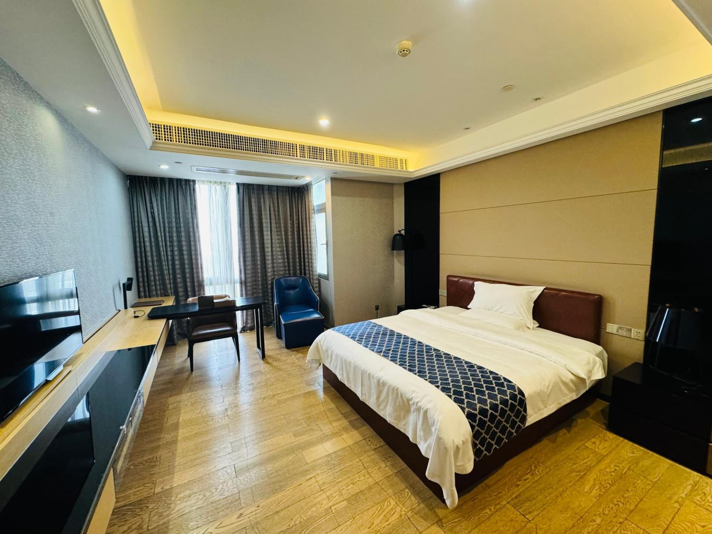 A hotel room with a large bed, a desk, a chair, and a TV.