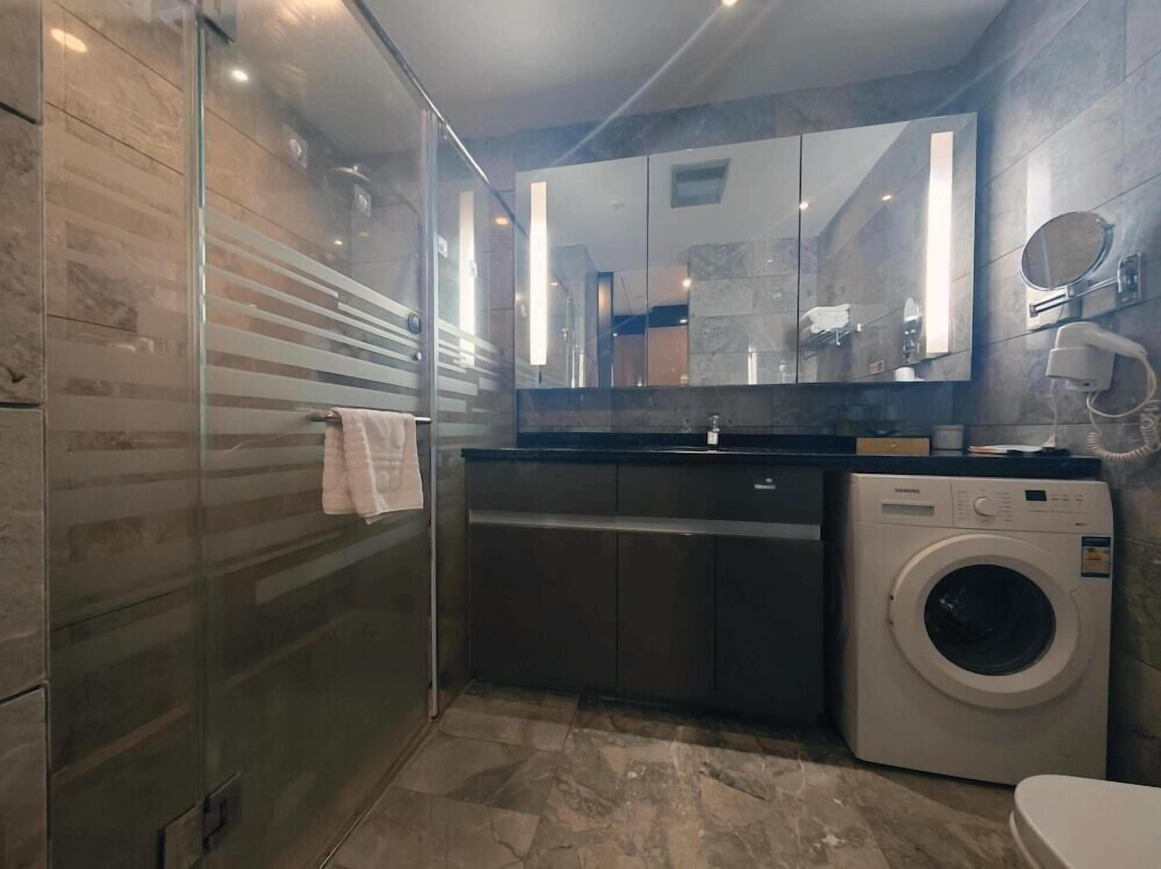 A modern bathroom with a glass shower enclosure, a built-in washing machine, and a large mirror above the sink.