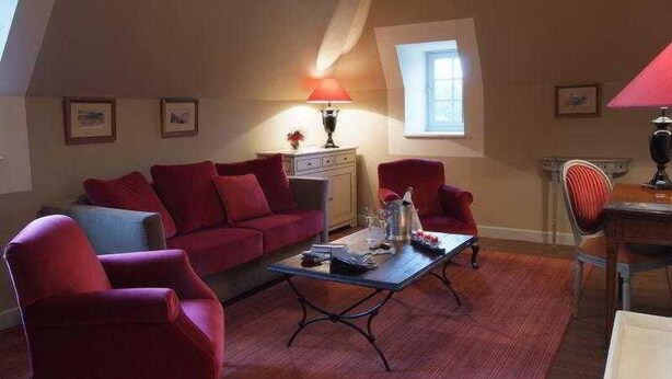 Una habitación con un sofá rojo, una mesa de centro, una lámpara, una mesita con un jarrón y una ventana.