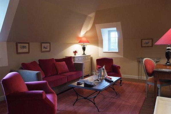 Une pièce avec un canapé rouge, une table basse, une lampe, une petite table sur laquelle se trouve un vase, et une fenêtre.