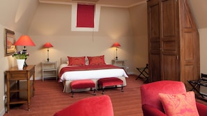 Un dormitorio con cama, dos lámparas de noche, un armario de madera, un sillón rojo y una pequeña mesa con un florero.