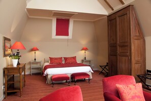 Une chambre à coucher avec un lit, deux lampes de chevet, une armoire en bois, un fauteuil rouge et une petite table sur laquelle est posé un vase de fleurs.