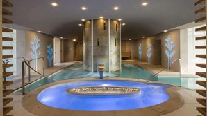 Un área de spa con un jacuzzi central, una piscina y una estructura de columna de piedra.