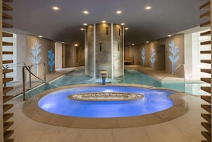 Un espace spa comprenant un grand bain à remous central, une piscine et une structure en colonnes de pierre.