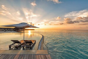 An infinity pool with lounge chairs and an umbrella, overlooking a calm sea at sunset. - Hurawalhi Island Resort Maldives (Huruvalhi)