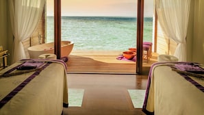 Ein Zimmer mit zwei Betten, einer Badewanne und einer Holzterrasse mit Meerblick.